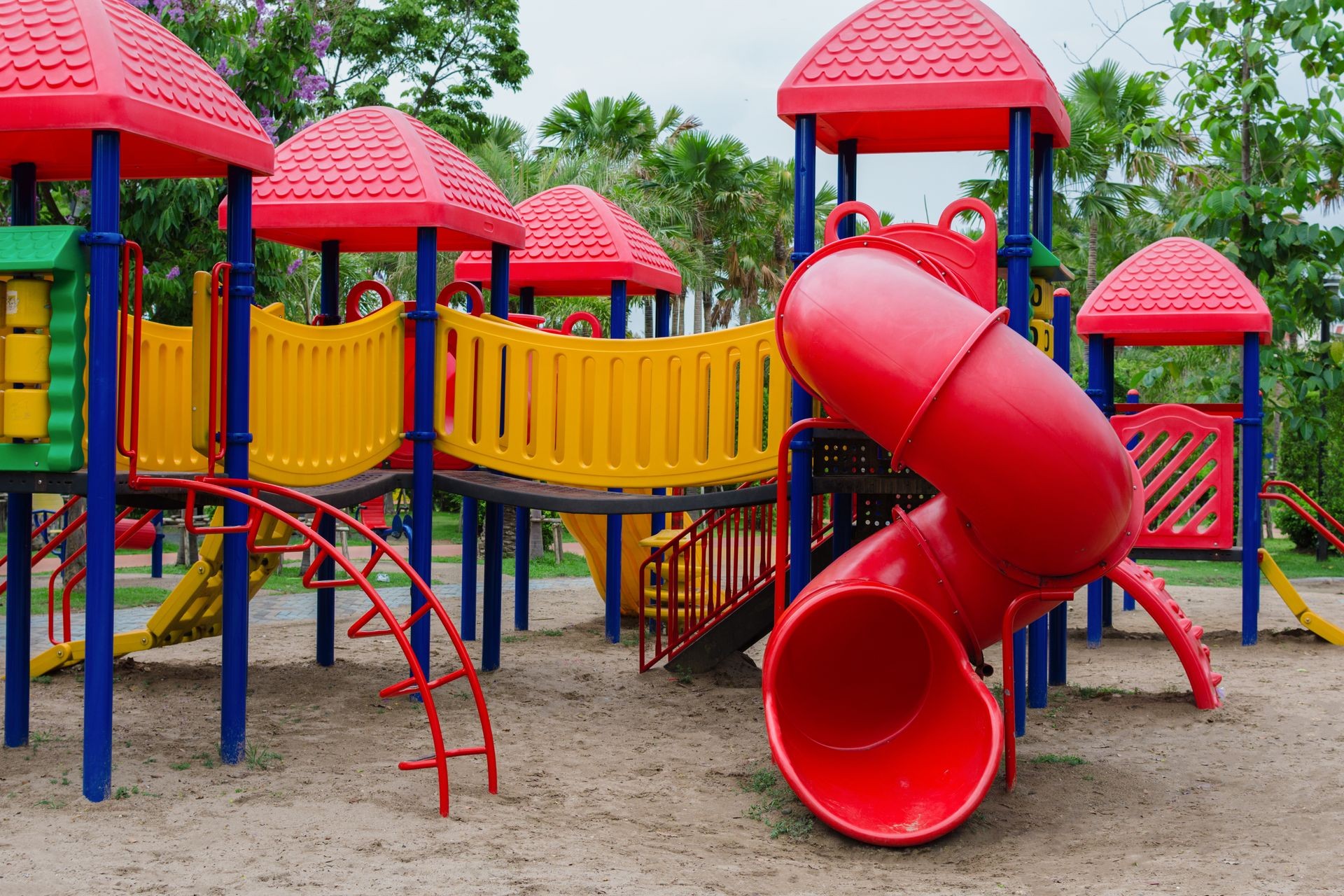 Colorful playground with red slides, yellow bridges, and green panels surrounded by trees.