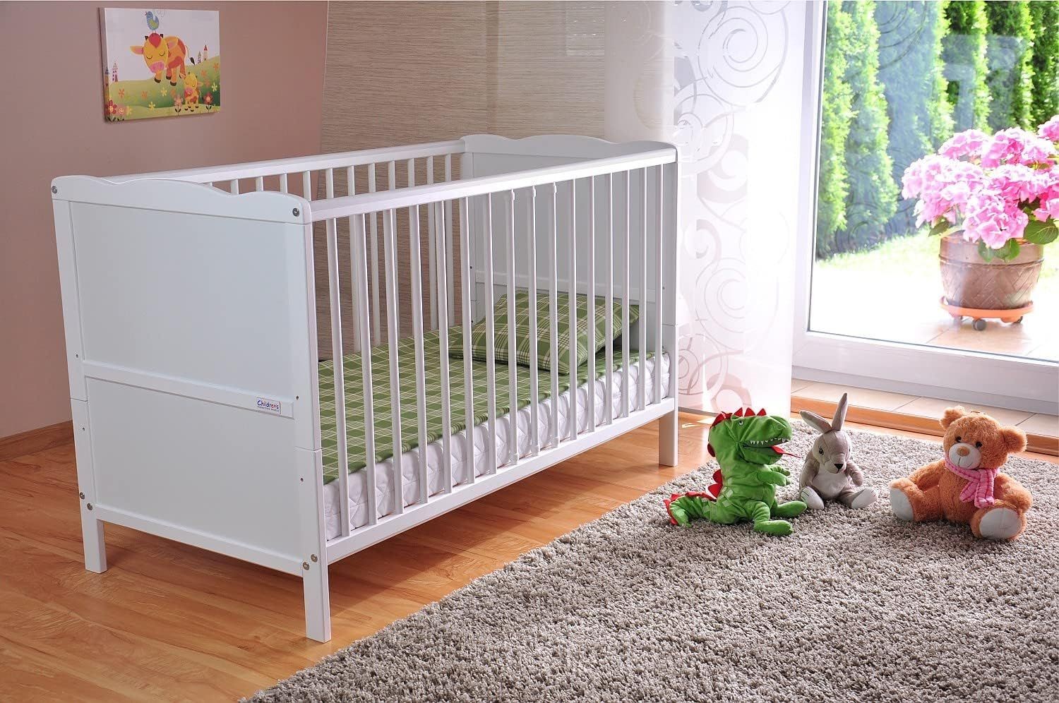 White crib with green bedding next to stuffed toys on a gray carpet in a bright nursery room.