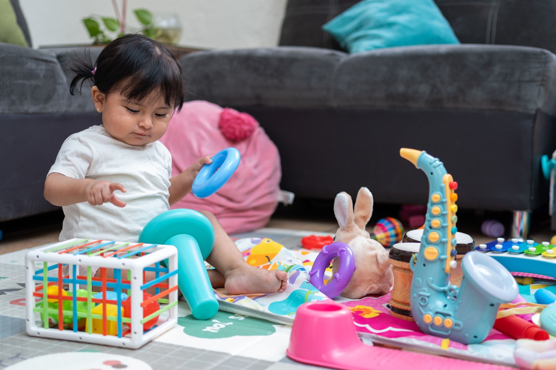 Hispanic toddler engaged in learning and motor skills development with educational toys in the living room, exploring shapes and sizes with a ring stacking toy